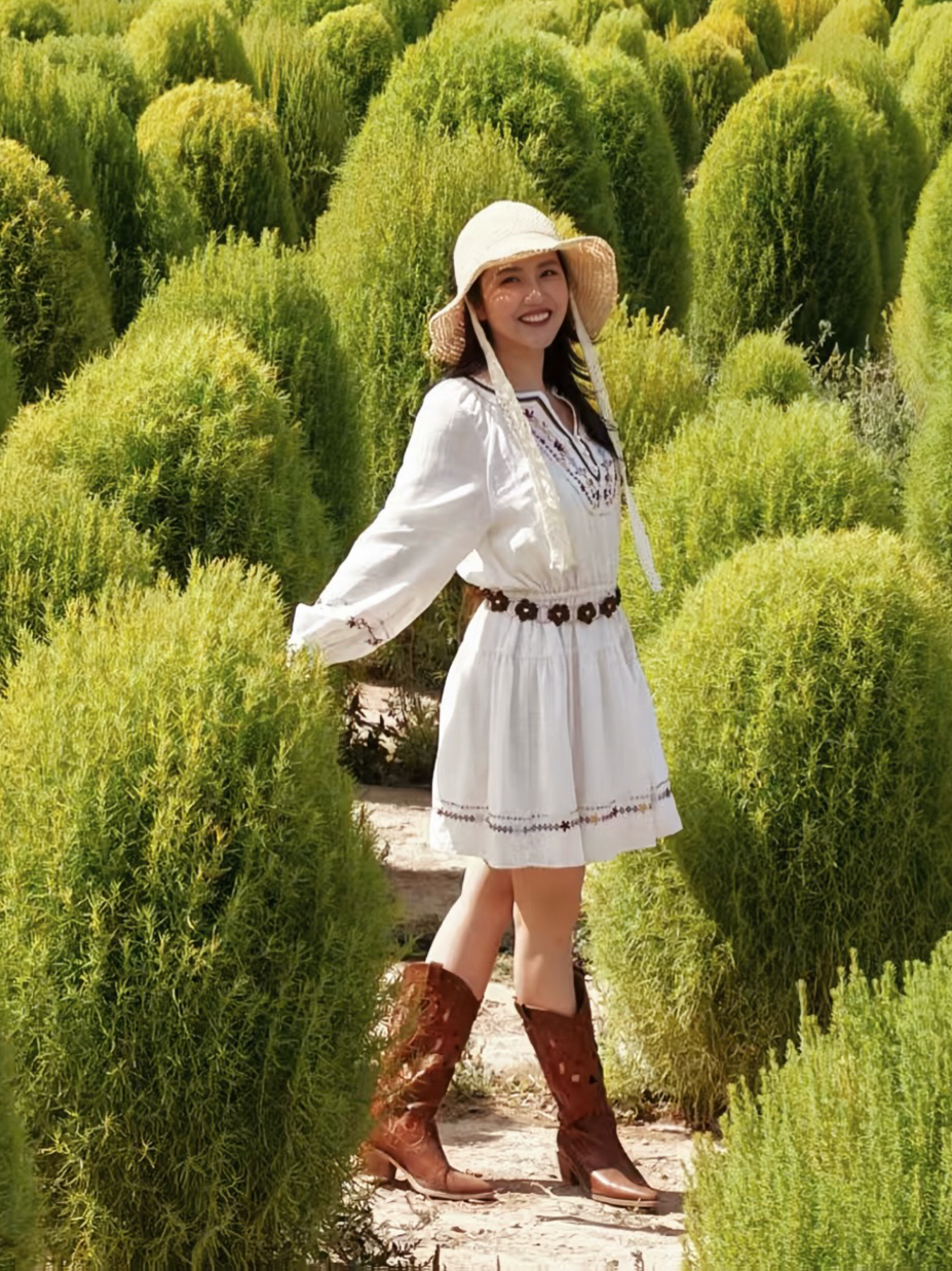 Tạo dáng giữa cánh đồng ở Tân Cương, Primmy Trương mặc đồ kiểu boho với váy xòe thêu họa tiết, đi cùng thắt lưng và boots da cùng mũ cói.