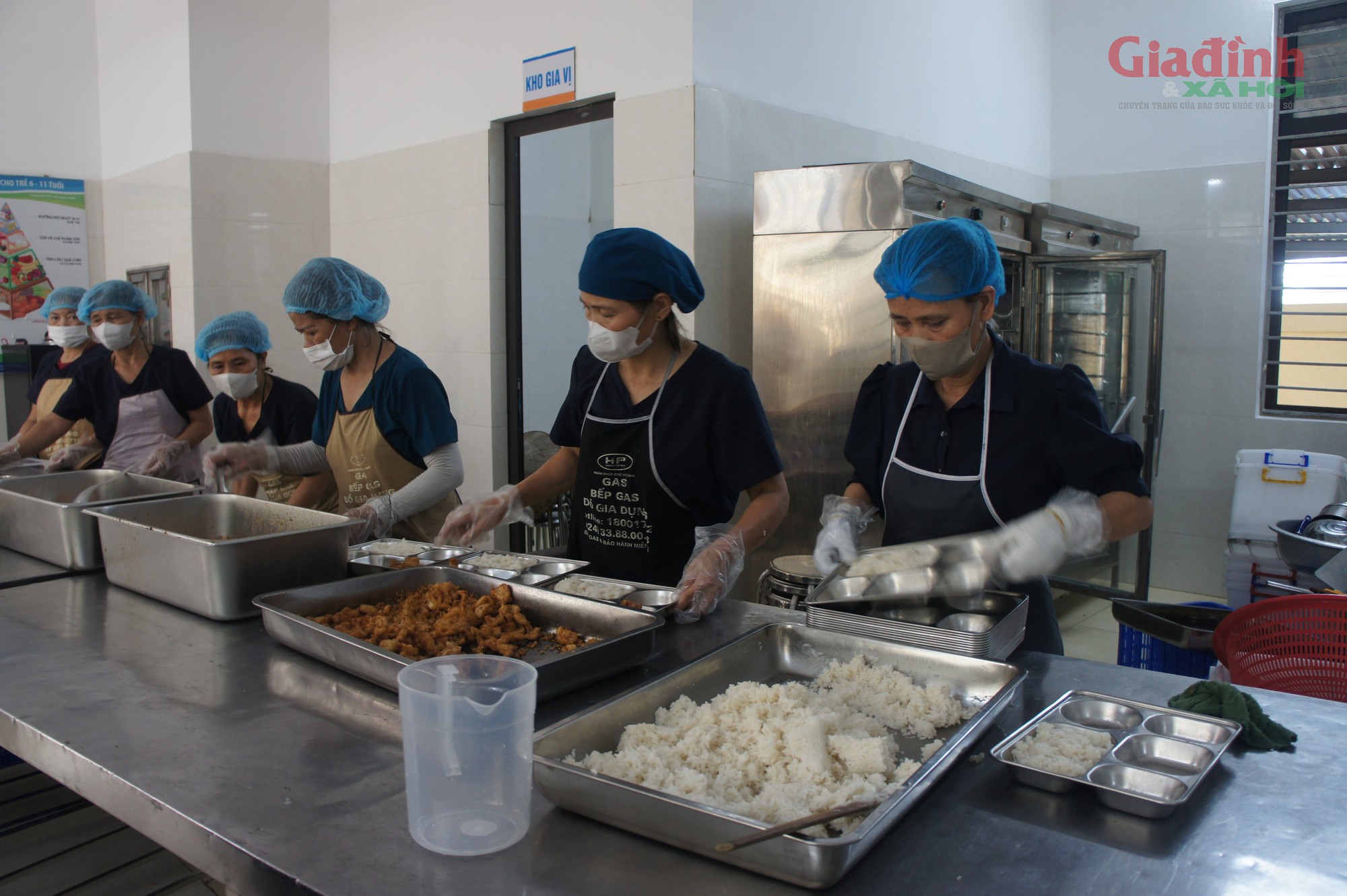 Tại khu vực bếp ăn trong khuôn viên trường Tiểu học Quảng Bị 1, từ khoảng 10h sáng, sau khi thực phẩm đã được nấu chín, các nhân viên nhà bếp bắt đầu cấp tập chia suất ăn. Nhân viên nhà bếp trang bị găng tay và khẩu trang, luân phiên nhau chia các món ăn chín vào từng khay cơm chuyên dụng.