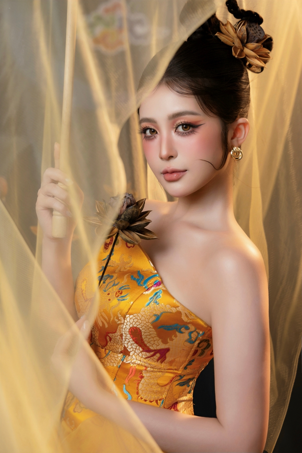 Thùy Trang rực rỡ trong thiết kế màu vàng đồng với họa tiết rồng, kết hợp kiểu tóc búi cao và phụ kiện lấy cảm hứng từ hoa sen, hạt sen.