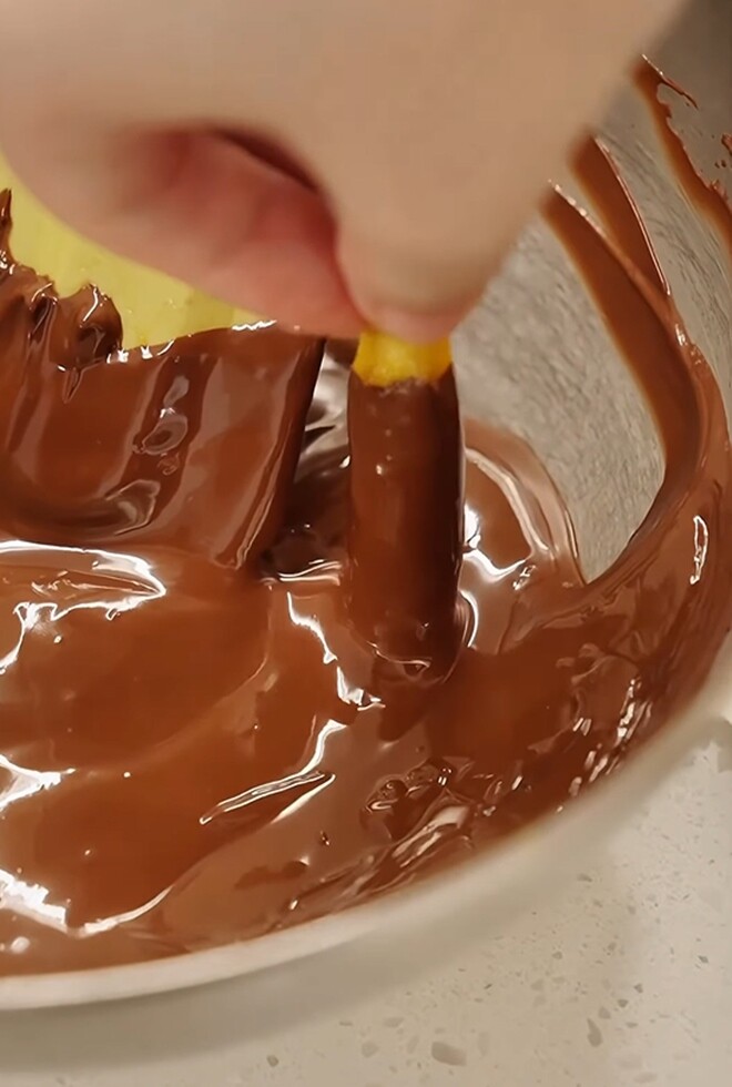 Từng miếng vỏ cam sên dẻo được nhúng ngập khoảng 3/4 chiều dài vào bát chocolate đun chảy một cách khéo léo.