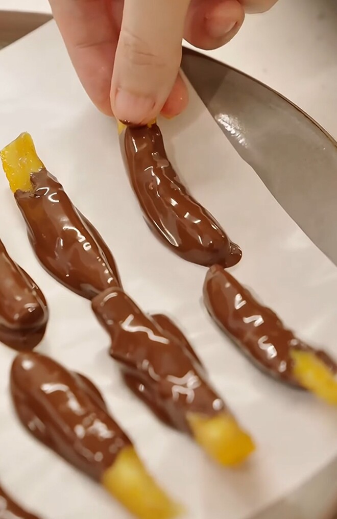 Những miếng chocolate nhân vỏ cam sau khi nhúng được xếp ngay ngắn lên lớp giấy nến để tránh bị dính và giúp tạo hình đẹp mắt hơn.