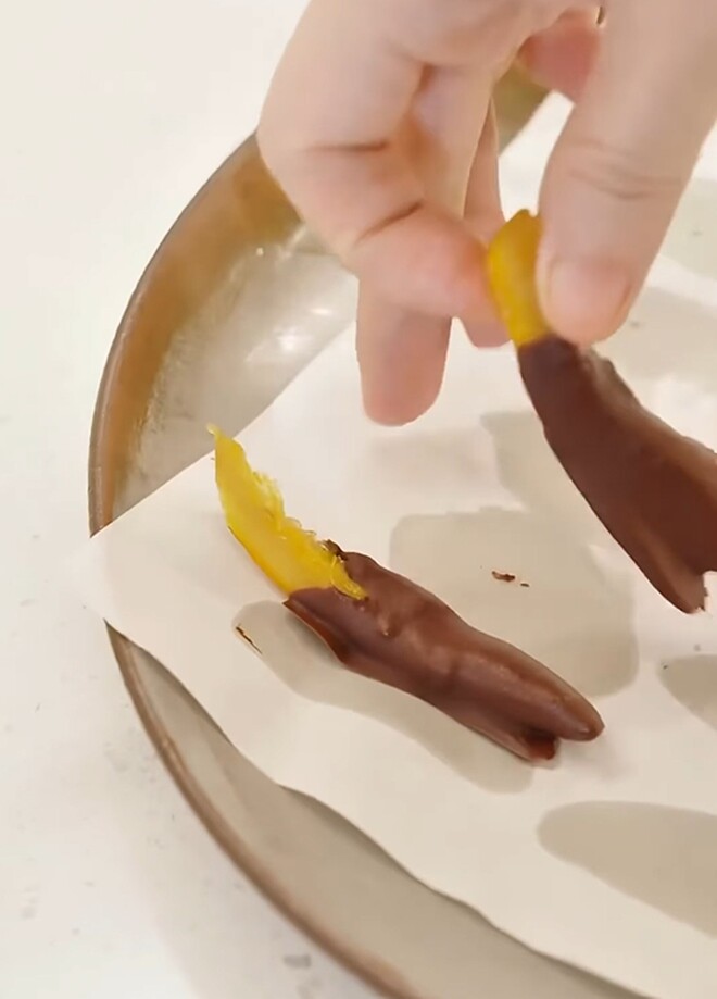 Cận cảnh một miếng chocolate nhân vỏ cam hoàn thiện với lớp vỏ nâu đen bóng bẩy bao bọc lấy phần nhân cam vàng ruộm bên trong.