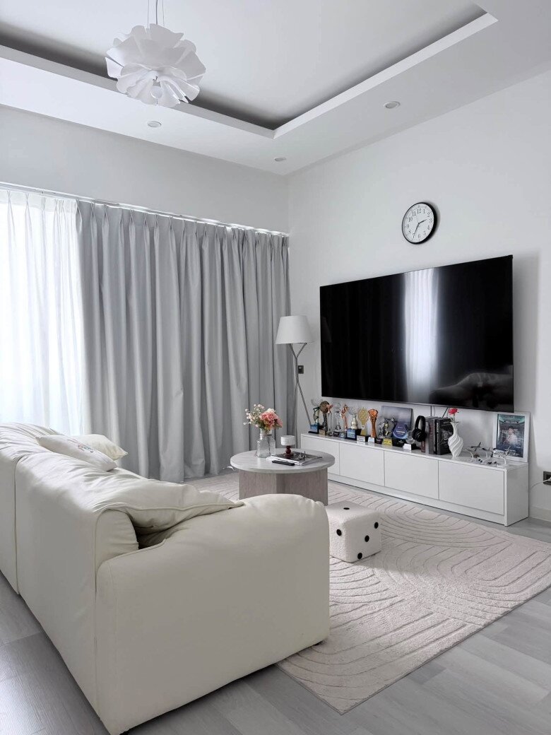 Kệ TV trắng nhã nhặn là nơi trưng bày hàng loạt cúp thưởng danh giá của cả hai vợ chồng. Chiếc đồng hồ treo tường đơn giản cùng thảm trải sàn dệt họa tiết uốn lượn tạo chiều sâu cho căn phòng.