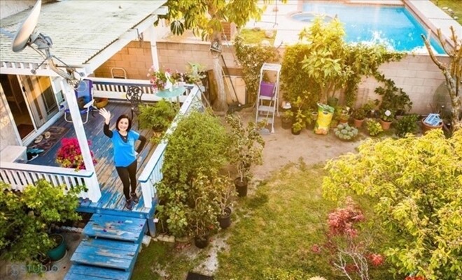 Toàn cảnh khuôn viên sống riêng tư với ban công gỗ màu xanh, khoảng sân cỏ rộng rãi và hồ bơi xanh mát phía xa. Ngôi nhà mang kiến trúc đậm chất nghỉ dưỡng, tràn ngập cây xanh và ánh nắng thiên nhiên.