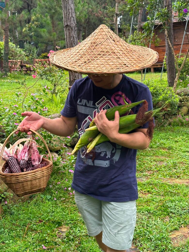Dù trời đổ mưa khiến đường đi trơn trượt, người nông dân Trọng Tấn vẫn tràn đầy năng lượng khi tự tay xách giỏ nông sản đi giữa lối nhỏ quanh co, xung quanh là đồi dốc tự nhiên được kè đá kiên cố, phủ đầy hoa.