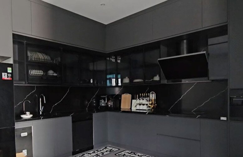 Cận cảnh góc bếp chữ L gọn gàng với mặt bếp và tường ốp đá xước đen vân mây sang trọng, vừa dễ dàng vệ sinh vừa mang lại tính thẩm mỹ cao. Mọi vật dụng nấu nướng được sắp xếp ngăn nắp, thể hiện sự chu đáo trong sinh hoạt của gia đình.