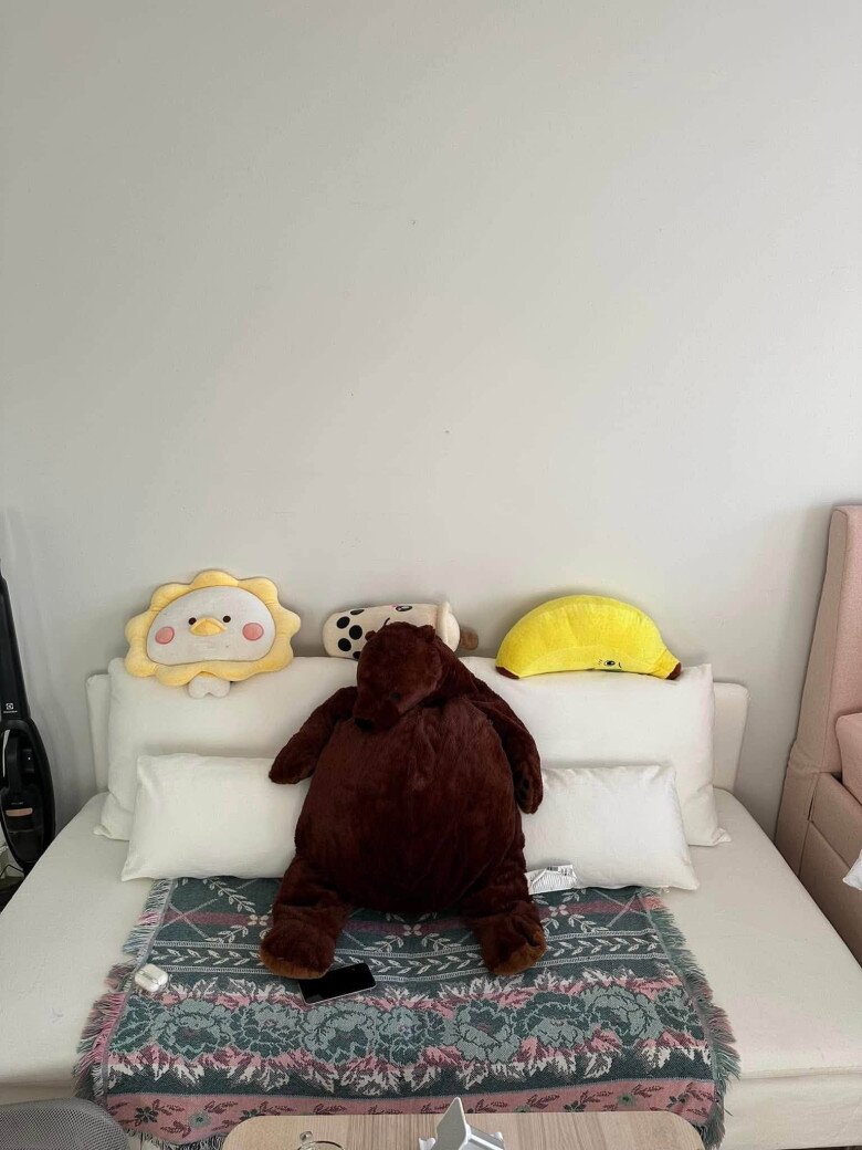 Một góc thư giãn khác trong nhà với chiếc ghế sofa màu trắng sữa êm ái, phía trên phủ tấm thảm thổ cẩm dệt họa tiết cổ điển sang trọng. Điểm nhấn của góc này là chú gấu bông nâu cỡ lớn và những chiếc gối hình thù ngộ nghĩnh, mang lại cảm giác thân thuộc, vui mắt.