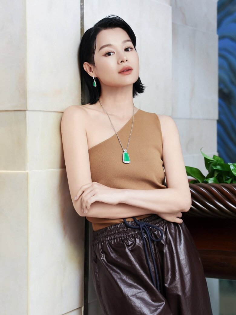 Kết hợp áo lệch vai màu nâu với quần da tối màu, Hồ Hạnh Nhi lựa chọn mặt dây chuyền ngọc lục bảo hình chữ nhật cùng đôi hoa tai đồng điệu. Sắc xanh nổi bật trên nền trang phục trung tính giúp tổng thể thêm quyền lực, tinh tế và cuốn hút.