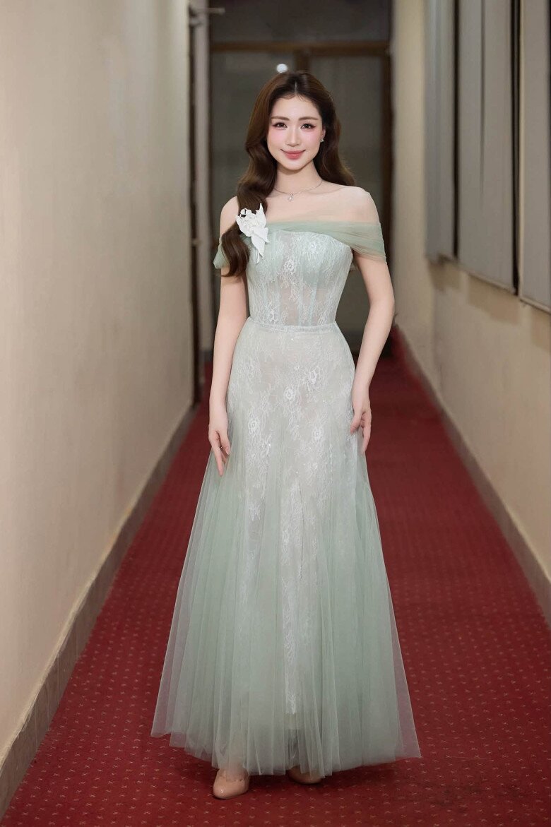 Hòa Minzy lựa chọn đầm voan tông xanh nhạt với phom cúp ngực, tạo cảm giác nhẹ nhàng và nữ tính. Điểm nhấn nằm ở phần vai trễ, cùng bông hoa trắng bản lớn đặt trên vai, giúp tổng thể trang phục thêm nổi bật. 