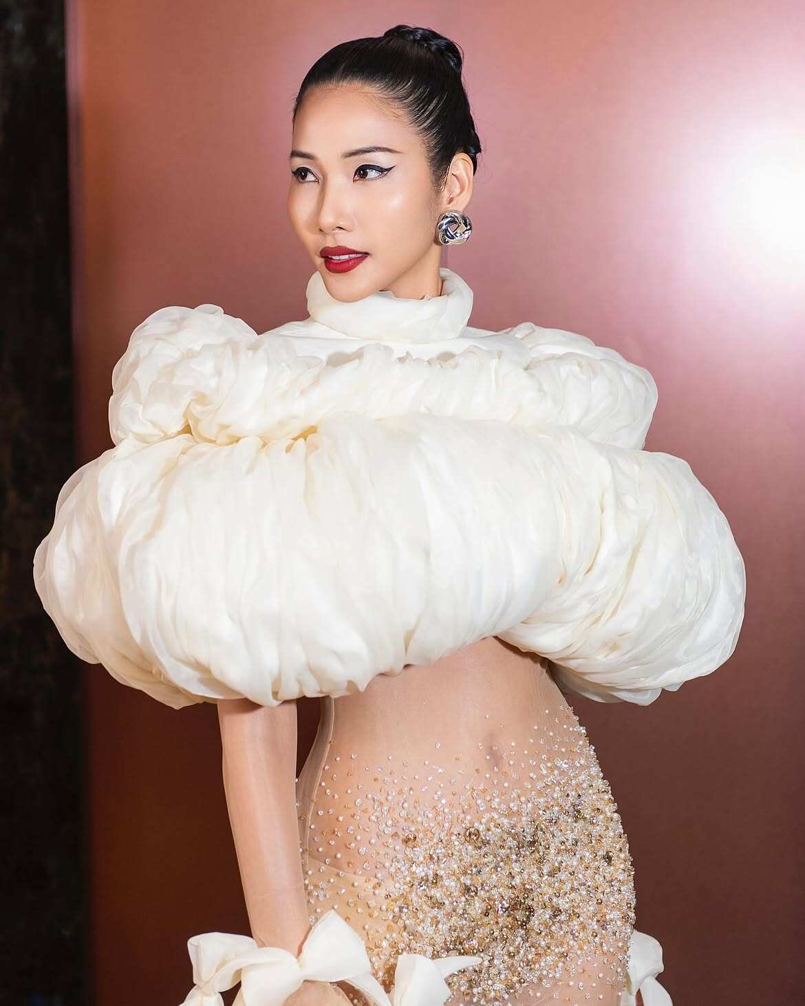 Một lần, Hoàng Thùy gây chú ý với thiết kế dạ hội trắng có phom thân trên bồng xòe, tạo điểm nhấn ở phần cổ cao và eo gọn. Phần chân váy xuyên thấu đính pha lê, ngọc trai giúp tổng thể thêm nổi bật. 