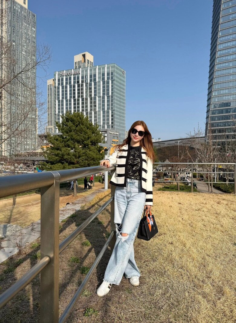 Xuống phố, Hạnh Sino diện áo khoác dạ dáng ngắn hai tông trắng - đen cùng quần jeans rách gối. Cô khéo mix amp; match bằng túi Hermès màu đen - hàng hiệu xa xỉ hàng đầu nước Pháp, điểm thêm khăn lụa họa tiết ở quai cầm, mang đến tổng thể vừa năng động vừa sang trọng.
