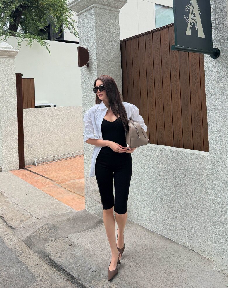 Một công thức khác được nữ ca sĩ áp dụng là sơ mi trắng oversized khoác ngoài bodysuit đen. Sự đối lập giữa phom rộng và thiết kế ôm sát tạo hiệu ứng cân bằng cho outfit. Trong khi đó, kính mắt đen, túi nâu bản lớn và giày cao gót mũi nhọn góp phần định hình vẻ ngoài cá tính.