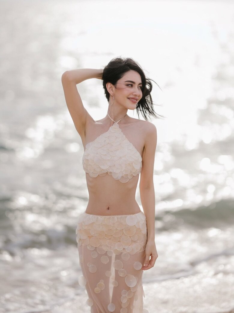 Ở một khung hình khác, Mai Davika tiếp tục gây chú ý với set đồ hai mảnh gam nude đầy táo bạo. Thiết kế áo yếm dáng croptop kết hợp chân váy xuyên thấu, được tạo nên từ hàng loạt chi tiết vảy cá mỏng nhẹ, tạo hiệu ứng lấp lánh như mặt biển dưới nắng.