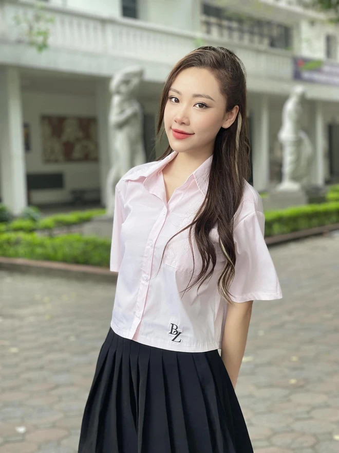 Một bản phối tiêu biểu là sơ mi hồng pastel dáng lửng kết hợp chân váy xếp ly màu đen. Sự tương phản giữa gam màu sáng và tối tạo hiệu ứng thị giác rõ ràng, trong khi phần áo ngắn giúp tỷ lệ cơ thể trông cân đối hơn. Lối trang điểm nhẹ và kiểu tóc tự nhiên khiến outfit mang đậm tinh thần đời thường.