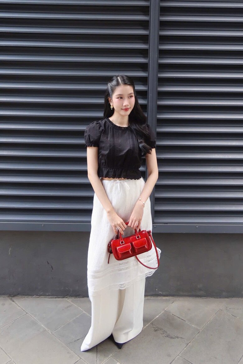 Á hậu Phương Anh cao tay khi kết hợp áo đen croptop và quần ống rộng trắng, tạo điểm nhấn ấn tượng với chiếc túi xách màu đỏ.