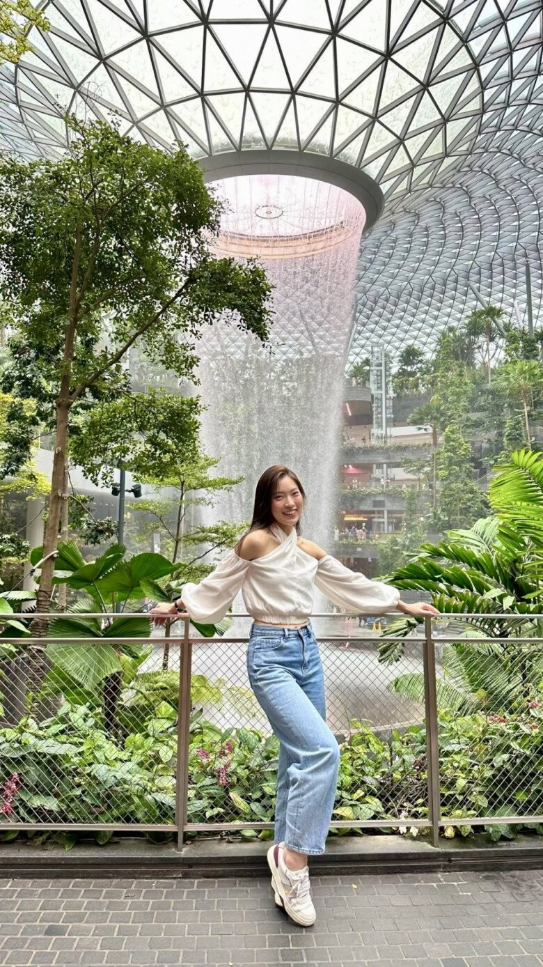 Người đẹp sinh năm 1999 chọn công thức phối đồ tối giản nhưng sành điệu, kết hợp chiếc áo trắng hở vai thiết kế đan chéo độc đáo và tay phồng nữ tính. Set đồ hoàn thiện với quần jeans ống rộng cạp cao và đôi sneakers năng động, tạo nên tổng thể trẻ trung, cá tính nhưng không kém phần thanh lịch.