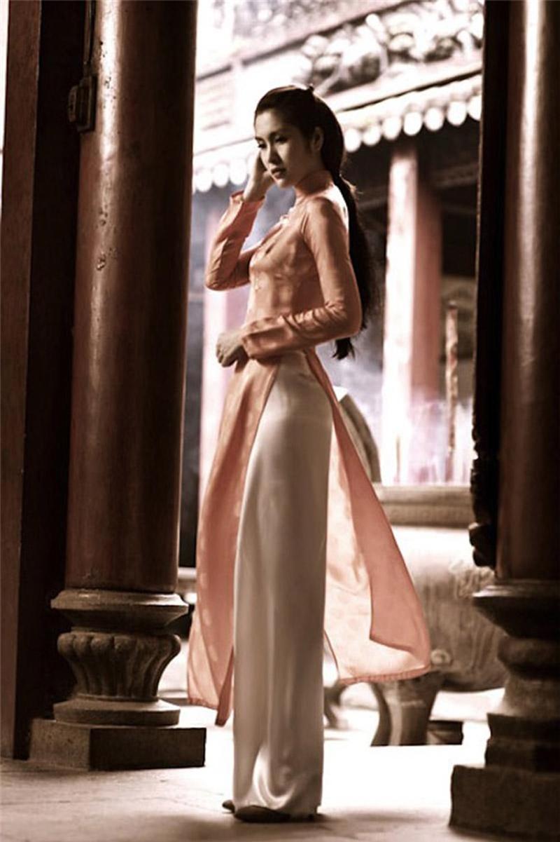 Áo dài gấm tông màu hồng phấn truyền thống, với phần tà ngắn nhưng kín đáo giúp cho người phụ nữ khoe triệt để hình thể. 
