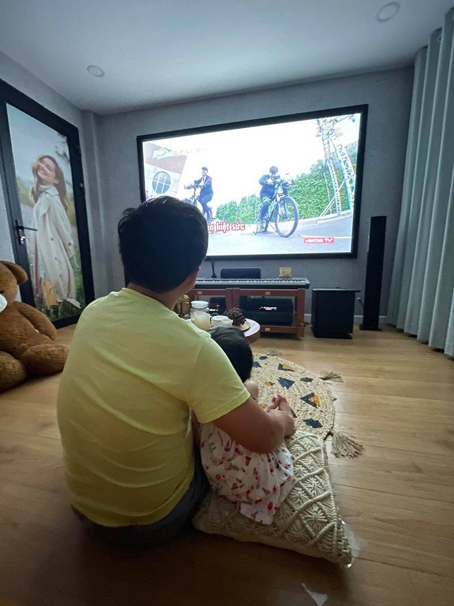 2 bố con quấn quýt, ngọt ngào ngồi trước màn hình tivi để theo dõi chương trình.