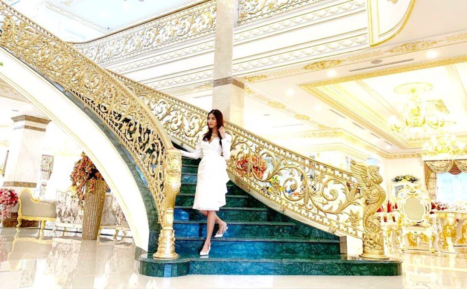 Lan Khuê tạo dáng tại cầu thang được chạm trổ tinh xảo. Nội thất biệt thự toát lên vẻ xa hoa, lộng lẫy với nhiều vật dụng, đồ trang trí dát vàng. Ảnh: FBNV.