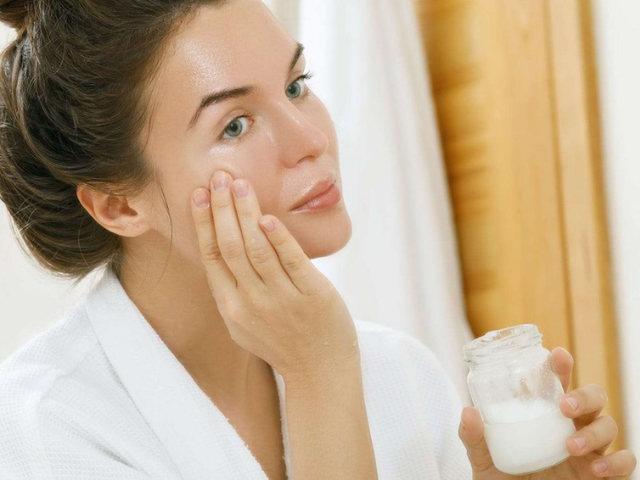 A woman applying milk to her face with a cotton pad