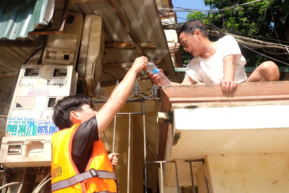 Nước ngập cả con phố và vẫn dâng cao quá nửa tầng một của các ngôi nhà khiến người dân buộc phải chuyển lên sinh hoạt tạm ở tầng hai. Sơn lớn bám hàng rào, rướn người lên để trao từng chai nước.