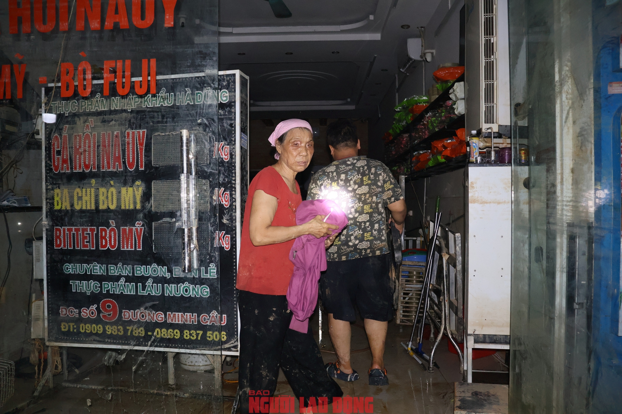 Một người dân đang thu dọn đống đổ nát trong nhà với gương mặt thẫn thờ. Toàn bộ cửa hàng cá hồi của gia đình đã bị trôi theo dòng nước lũ.