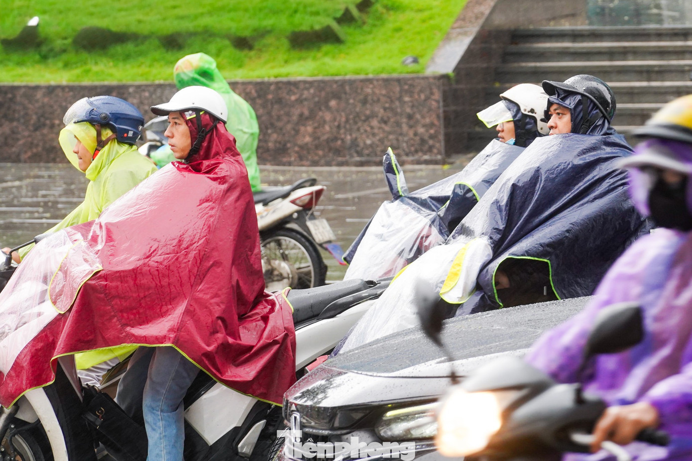 Gió lạnh thổi mạnh, áo mưa phồng lên theo từng cơn gió, người đi đường chật vật giữa mưa rét đầu ngày.