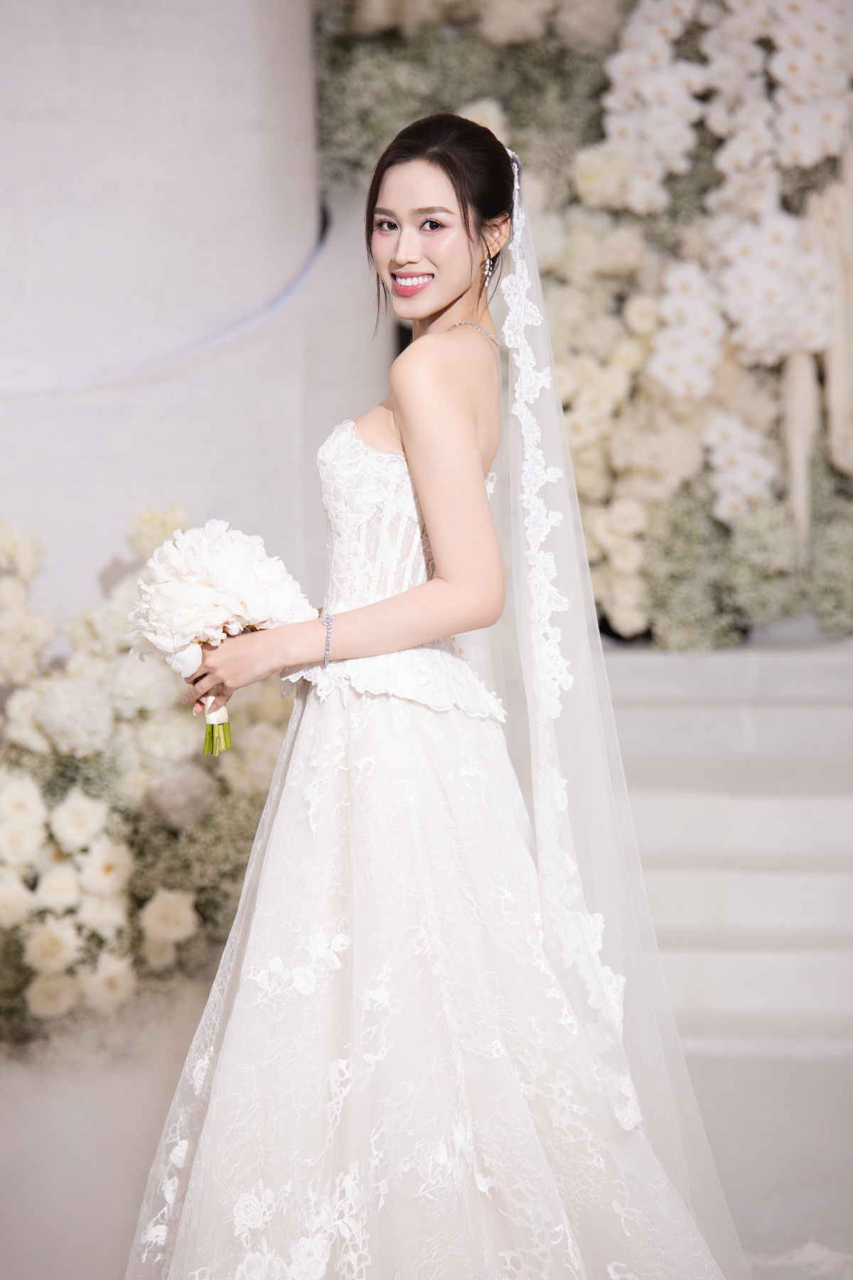 Tiếp tục ứng dụng phom corset siết eo trên nền chất liệu ren mỏng manh, NTK Phương Linh khéo xử lý để giúp Đỗ Thị Hà tôn ngực đầy và vòng eo con kiến. Chiếc váy được chỉnh sửa nhiều lần, nhằm phù hợp với cân nặng, số đo thay đổi của hoa hậu trước lễ cưới.