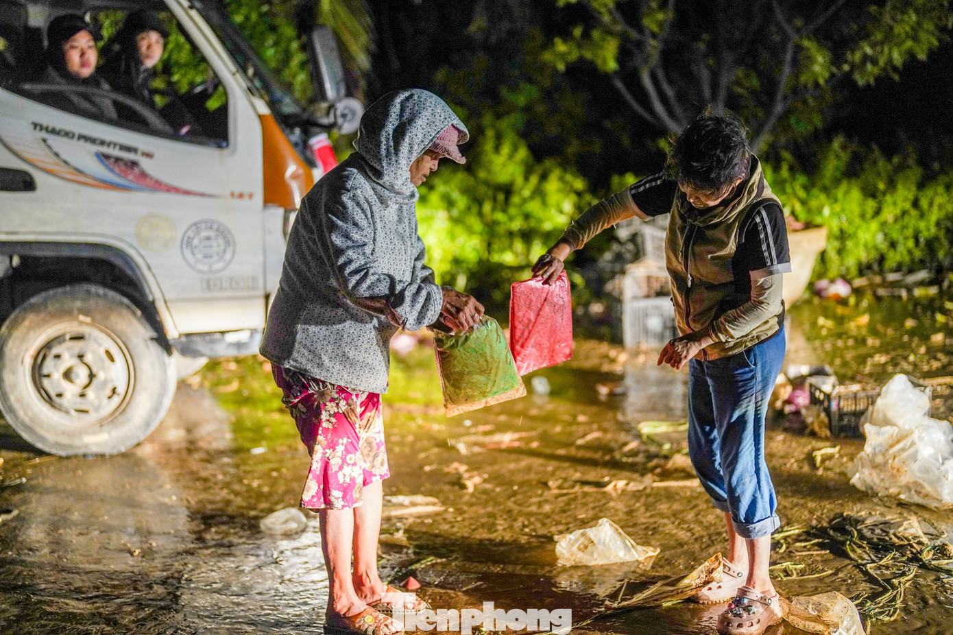 Sau khi xe hàng di chuyển, người dân vẫn cúi nhặt lại những phần quà không may bị rớt xuống bùn, cho thấy sự trân trọng và cần thiết của những món đồ cứu trợ.