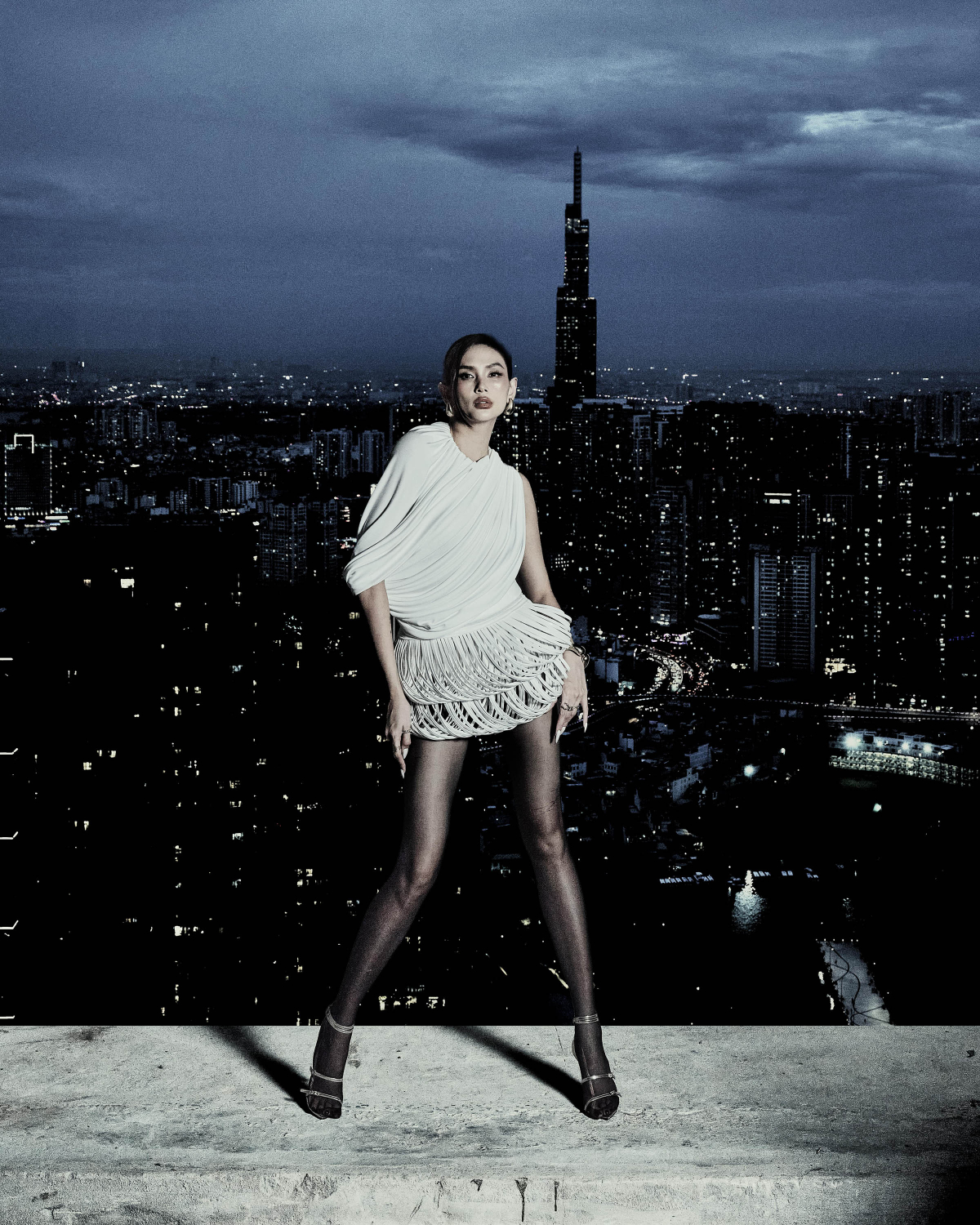 Thiết kế đầm ngắn giúp Võ Hoàng Yến tôn cặp chân thon dài. Phần thân trên với chất liệu thun được xử lý draping tỉ mỉ, tạo độ rủ tự nhiên và làm nổi bật cấu trúc vai bất đối xứng. Còn tùng váy được đan thủ công từ sợi da simili, mang lại hiệu ứng phồng tầng độc đáo.