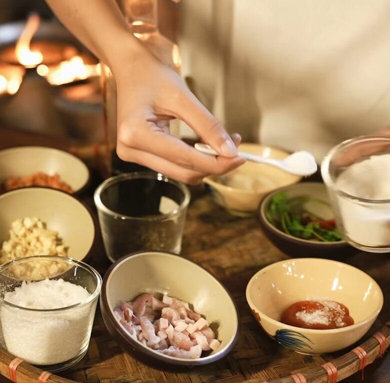 Người vợ xinh đẹp của nam ca sĩ cẩn thận đo lường từng muỗng gia vị, chuẩn bị nguyên liệu từ thịt ba chỉ, tỏi, hành, ớt đến các loại rau thơm, cho thấy sự chỉn chu trong từng món ăn.