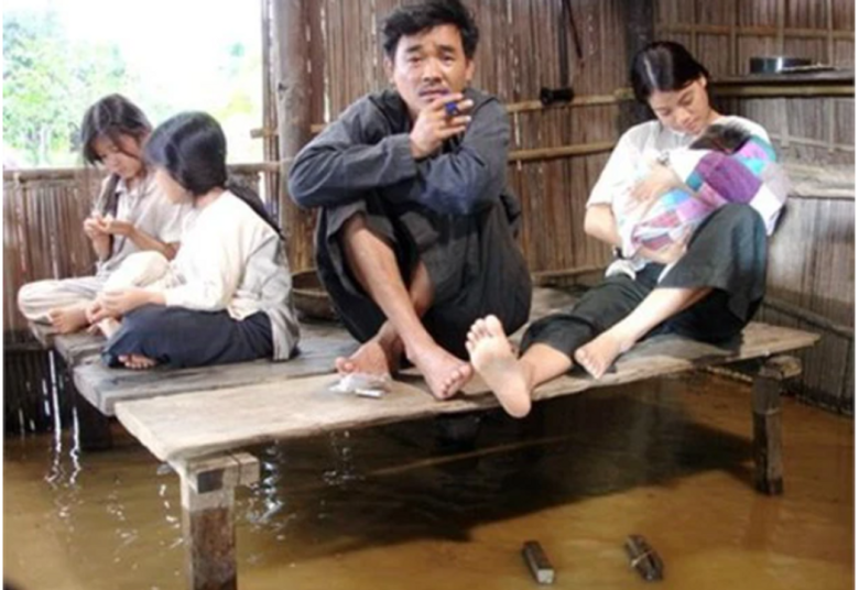Cảnh phim huyền thoại khi Gù ngẩn ngơ bất lực, ngồi co chân trên chõng, dưới đất là nước mưa dềnh lên.
