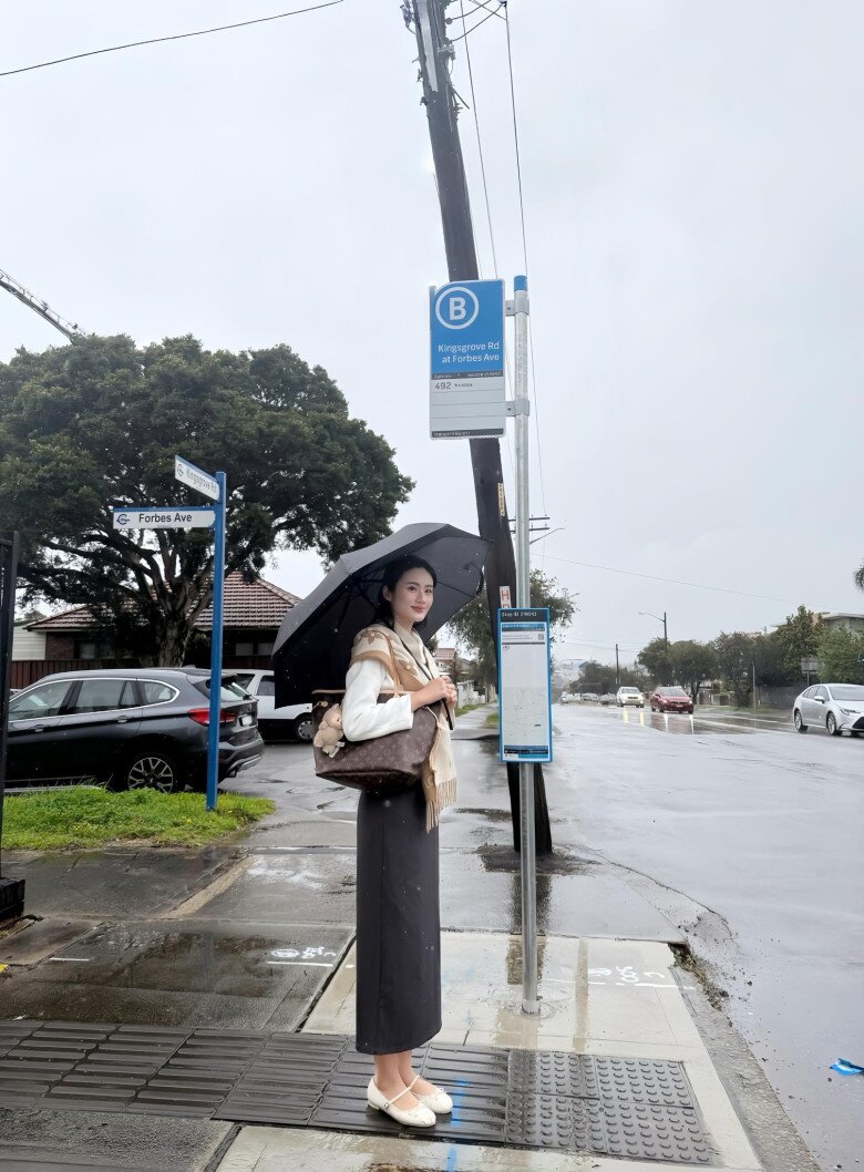 Ý Nhi khoe set đồ đi học ngày mưa với các gam màu trung tính. Hoa hậu phối áo khoác cùng chân váy bút chì chất liệu dạ ấm áp, phù hợp với thời tiết Sydney ngày đông. Người đẹp chọn phối thêm phụ kiện nghìn USD của Louis Vuitton là khăn quàng họa tiết Monogram.