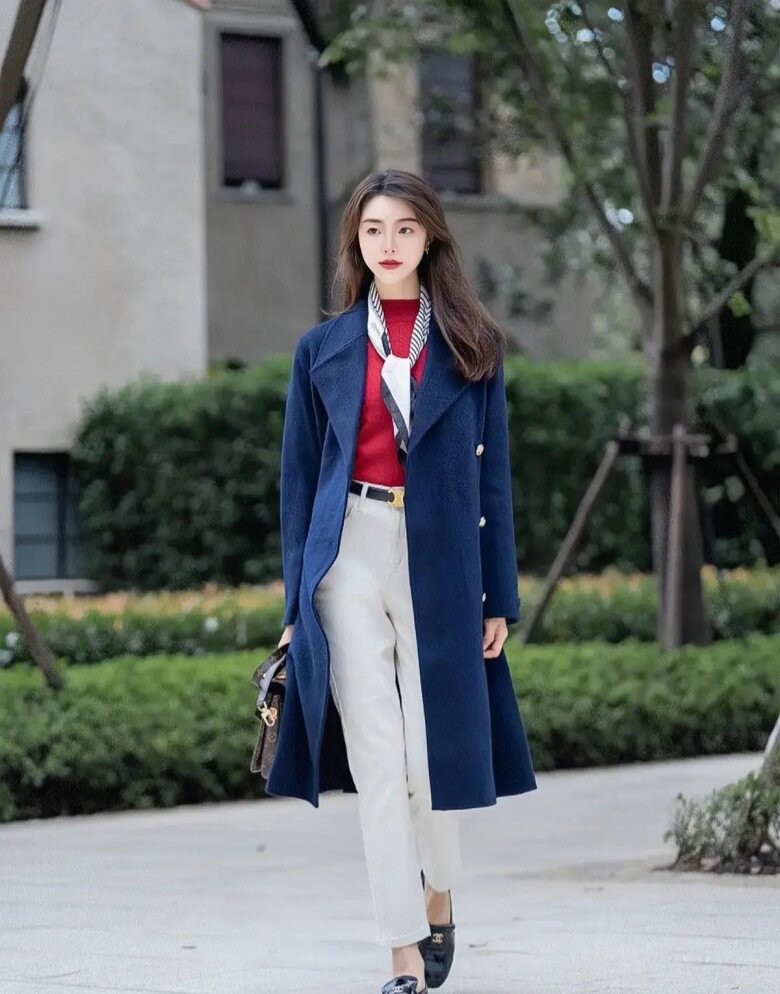 Set đồ nổi bật với áo khoác dáng dài màu xanh hải quân thanh lịch. Gam xanh trầm tạo cảm giác sang trọng, dễ phối khi kết hợp cùng áo len đỏ bên trong và quần trắng ống đứng, mang đến tổng thể gọn gàng, hiện đại và rất “tây”.