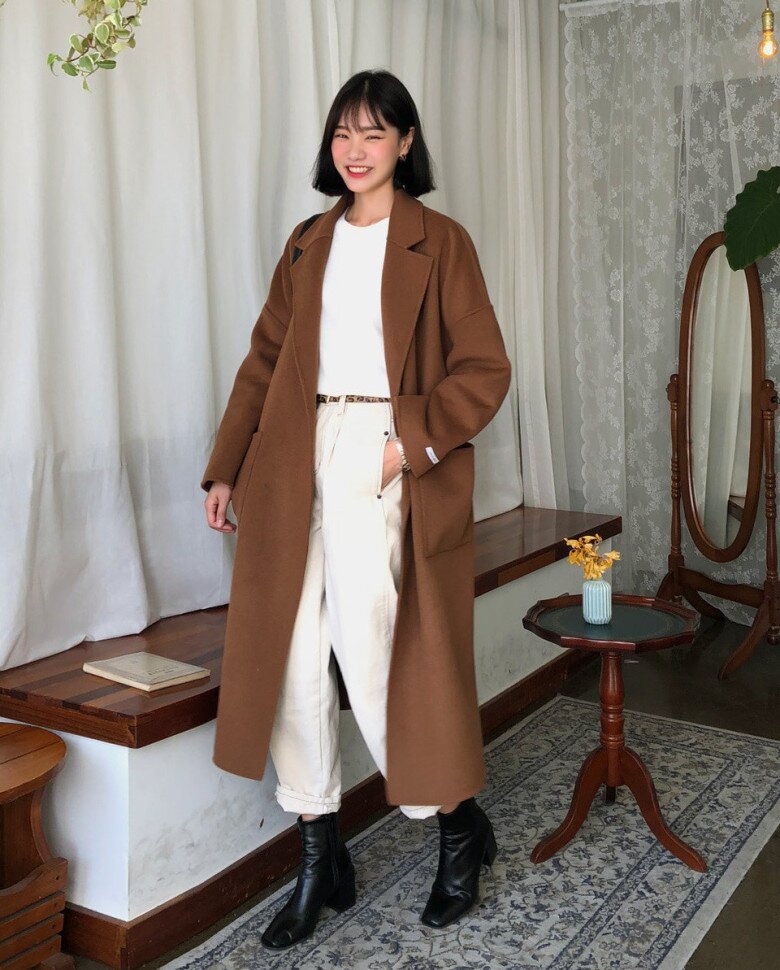 Phong cách thanh lịch, cổ điển với áo măng tô dáng dài màu caramel, phom áo rộng vừa phải tạo cảm giác chững chạc và thời thượng; sắc nâu ấm kết hợp cùng trang phục sáng màu bên trong giúp tổng thể cân bằng, nhã nhặn.