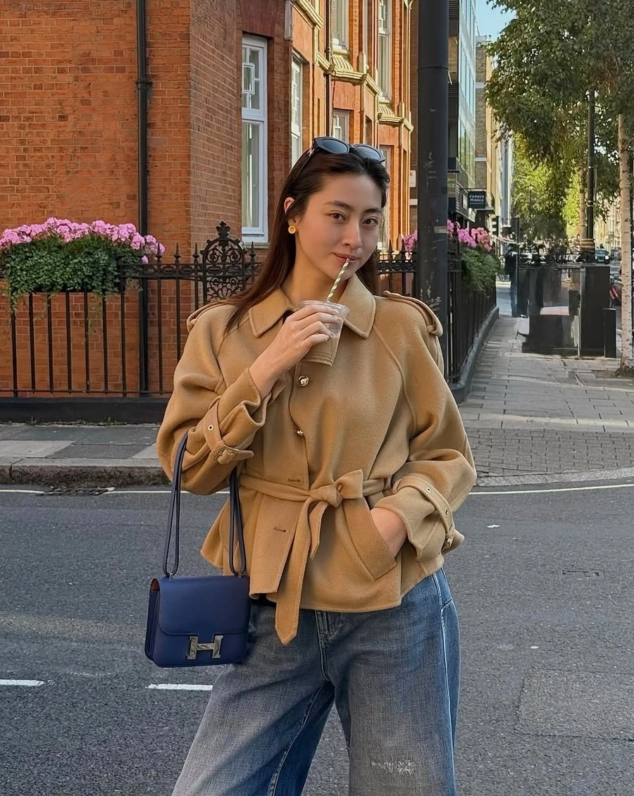Cũng lựa chọn áo trench coat, hoa hậu Lương Thùy Linh lại ghi điểm với phiên bản trench coat dáng ngắn bằng len, gam be đậm. Khi kết hợp cùng quần jeans và túi Hermès, sự hòa quyện giữa sắc be và denim mang đến tổng thể cá tính, trẻ trung và hiện đại.