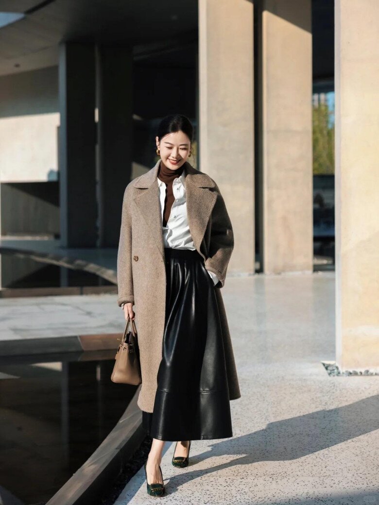 Hơi thở sang trọng đậm chất công sở hiện lên rõ nét qua bộ đôi áo khoác dạ màu caramel và chân váy midi da đen. Chất liệu da bóng nhẹ tạo chiều sâu tương phản với bề mặt lông dạ mềm mịn của áo khoác, mang đến vẻ ngoài tinh tế, chững chạc.