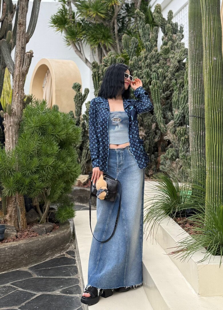 Trong khung cảnh ngập tràn cây xương rồng miền nhiệt đới, Lệ Quyên mang đến một diện mạo trẻ trung và phóng khoáng. Cô chọn áo pijama của Louis Vuitton màu navy in monogram để làm áo khoác ngoài, phối cùng áo crop-top dáng bandeau và chân váy denim dáng dài.
