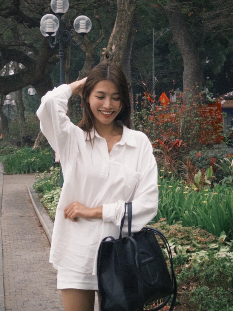Quỳnh Châu diện áo sơ mi trắng oversize kết hợp chân váy ngắn trắng, tạo tổng thể trẻ trung và tối giản. Cô chọn túi tote đen kích thước lớn của Telfar có giá từ 3,9 triệu đến 6,7 triệu đồng làm điểm nhấn giúp cân bằng gam màu sáng của trang phục.