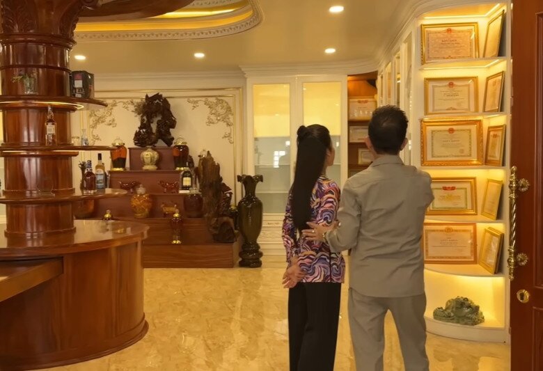 Phòng khách ở tầng hai có quầy bar nhỏ, nơi trưng bày bộ sưu tập rượu và tượng gỗ mỹ nghệ, bài trí tinh tế, vừa truyền thống vừa hiện đại. Trên tường trưng bày giấy khen và bằng khen của các thành viên trong gia đình, mang lại cảm giác tự hào và ấm cúng.