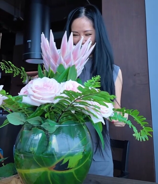 “Với một lọ hoa mà trong suốt thì thường là mình sẽ đổ nước vào trong và lấy cái lá ở ngoài vườn để xung quanh, để giấu đi miếng cát xanh ở giữa”, Hồng Nhung tiết lộ. Bình thủy tinh được che khéo léo bằng lá trầu bà, tạo nền xanh tự nhiên.