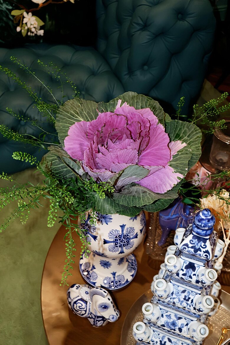 Cận cảnh hoa bắp cải tím nở đều, từng lớp cánh xếp lớp như hoa mẫu đơn, được nâng đỡ bởi phần lá xanh tươi và xốp cắm giấu kỹ trong bình sứ.