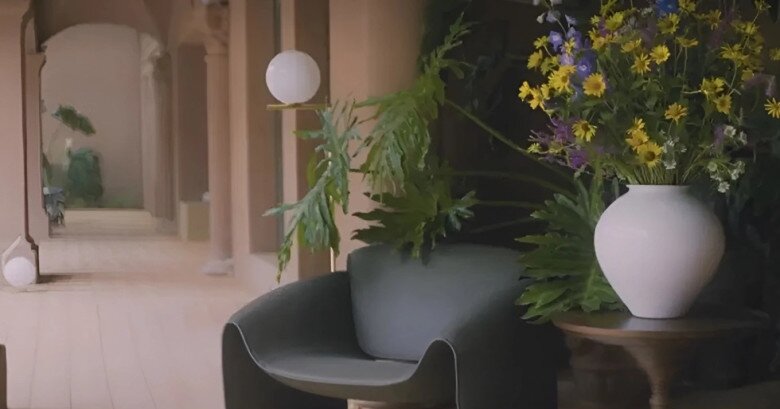 Hành lang dài lát gỗ sáng, điểm nhấn là các chậu cây, ghế đơn và bình hoa khổng lồ mang màu sắc tươi mát. Kiến trúc vòm tạo chiều sâu và cảm giác thư thái.