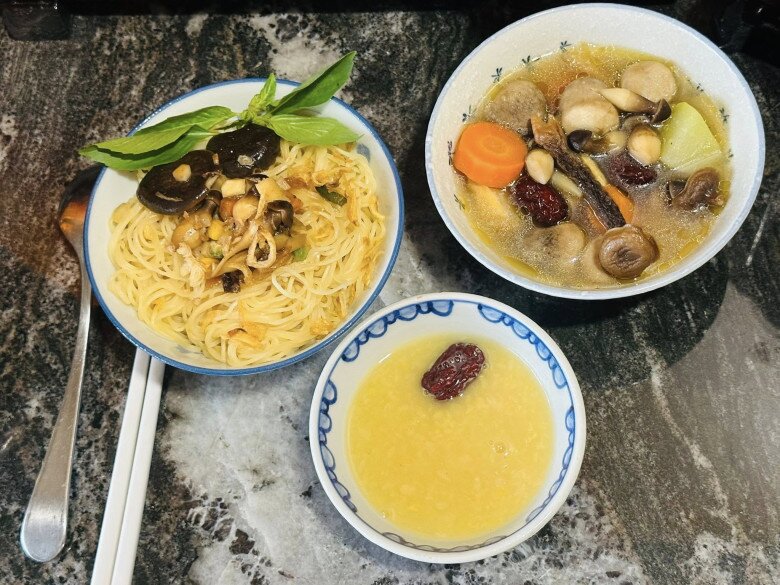 Món mì khô chay được trình bày công phu, với mì sợi vàng ươm, trang trí bằng nấm đông cô thái lát, nấm mèo và rau quế tươi. Đi kèm là một chén canh chay thập cẩm giàu dinh dưỡng gồm cà rốt, táo tàu, nấm các loại, cho thấy sự chu toàn của người con trai.