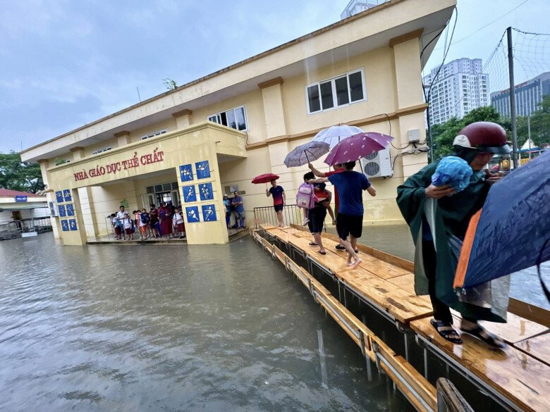 Một trường tiểu học ở Cầu Giấy kê bàn để học sinh và phụ huynh lội qua khu vực ngập.