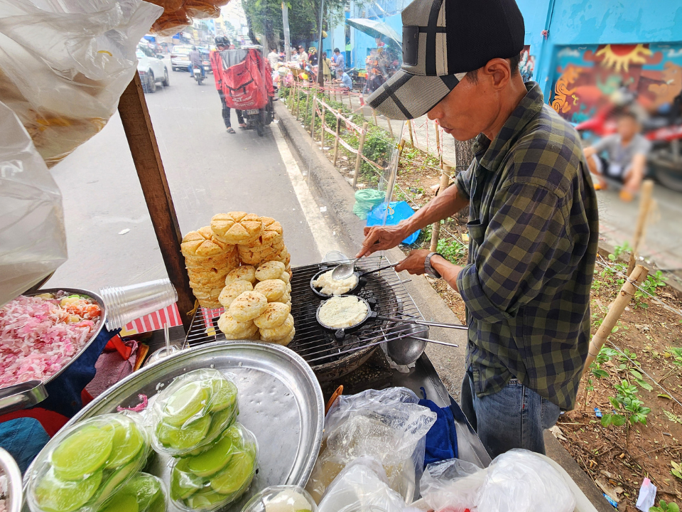 Trong lúc tâm sự, đôi tay anh vẫn tất bật chăm chút cho từng mẻ bánh nướng của mình. Động tác thuần thục, đều đặn như hơi thở: xoay khuôn, trở mặt bánh, rưới thêm chút nước cốt dừa cho mềm, rồi xếp ngay ngắn vào khay.