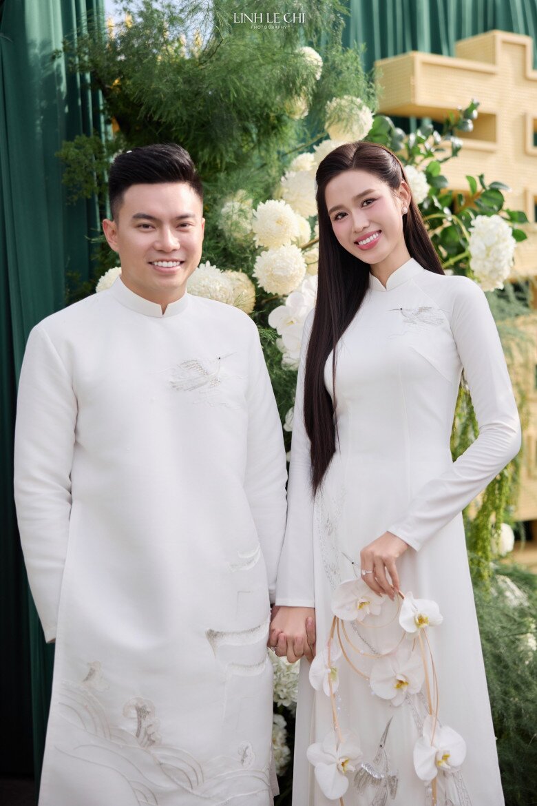 Chiếc áo dài Thanh Bình Hỷ Lạc được may riêng theo câu chuyện tình yêu của Hà và chú rể Viết Vương. Tông trắng sang trọng, hoạ tiết chim hạc tinh tế gợi hình ảnh bình an, hạnh phúc. Nàng hậu tinh tế chọn giày thấp, giữ nét hài hoà, dịu dàng trong ngày trọng đại.