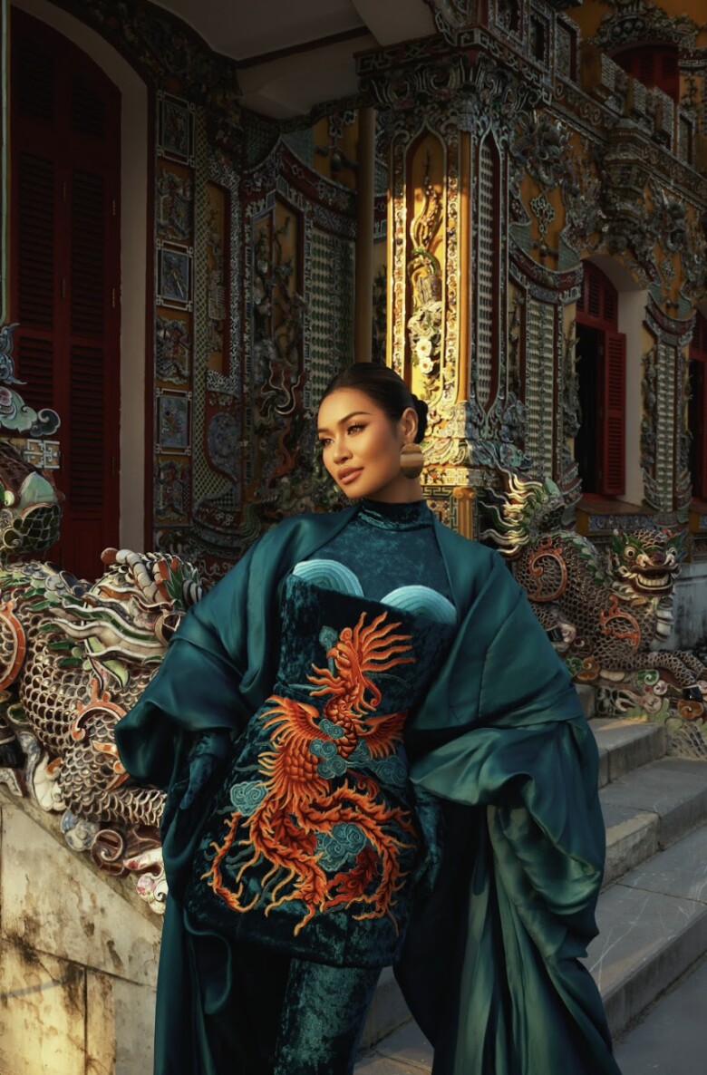 Á hậu Mook Karnruethai Tassabut nổi bật với trang phục nhung thêu rồng phượng tinh xảo, sắc xanh quyền uy. Điểm nhấn trong bức ảnh chính là thần thái lạnh lùng và ánh mắt sâu cuốn hút của mỹ nhân người Thái Lan.